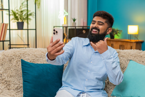 印度男子对着手机摄像头微笑自拍，发布照片到社交媒体，室内欢乐时光图片下载