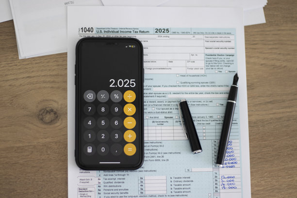 1040税表和智能手机照片。智能手机屏幕显示“2025”。税收年度和纳税概念。图片下载