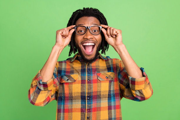 照片：一位英俊的深肤色男性，穿着格子衬衫，张大嘴巴笑着，背景是孤立的绿色图片下载