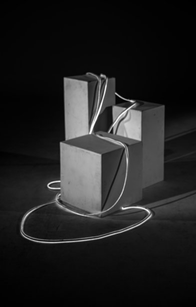 一张黑白照片，展示了一个艺术装置，其中几何色块在强烈的光线下，被一根发光的绳子优雅地连接在一起。图片下载