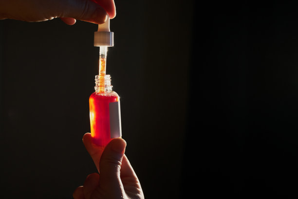 用滴管从美容产品瓶中提取红色液体精华液的手图片下载