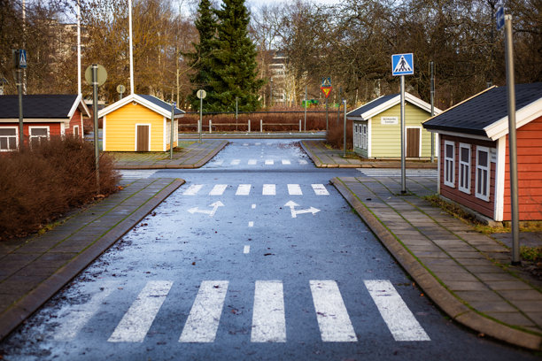 照片展示了一个大型儿童游乐场，旨在教授交通规则。孩子们在微缩街道上驾驶小型汽车，街道上设有交通标志和斑马线。非常适合教育主题、道路安全宣传、儿童活动和家庭友好视觉内容。图片下载