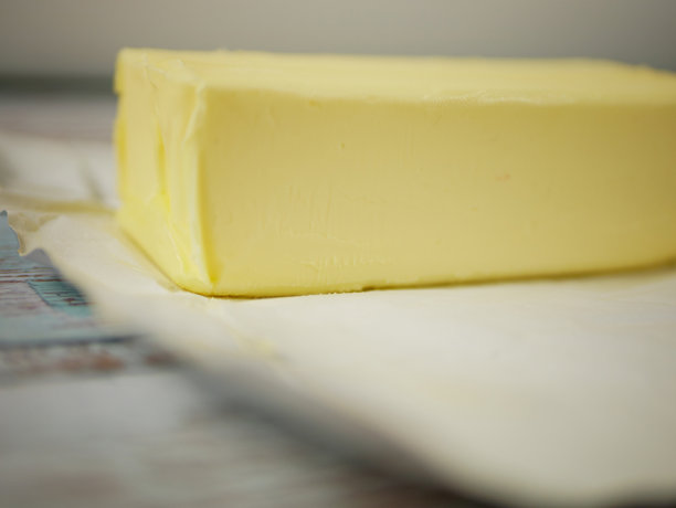 一块黄油放在打开的白色包装纸上，置于乡村风格的木桌上，这是一张简单的乳制品食材照片，适用于经典的家庭烹饪和烘焙食谱设计，步骤清晰。图片下载