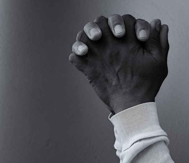 一名加勒比男子在黑色背景前合掌祈祷，身后有人群的素材照片图片下载