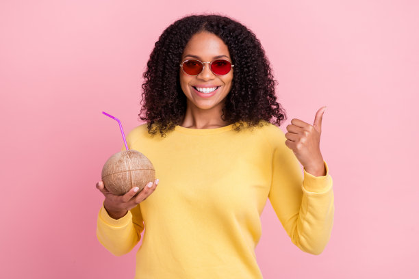 穿着黄色毛衣、戴着眼镜、手拿笔记本的闪亮、肤色黝黑的女性，在粉色背景下拍摄的照片图片下载