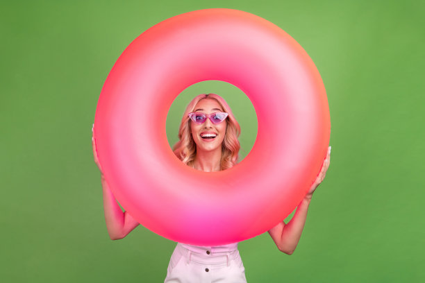 照片：一位美丽的女子微笑着，手持游泳圈，在泳池派对上享受夏日周末，背景为绿色。图片下载