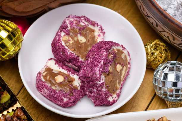 玫瑰花瓣和坚果的土耳其软糖卷放在白色盘子上，旁边有圣诞装饰品。图片下载