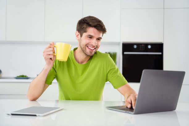 在家中，一名男子坐在厨房里，一边喝咖啡一边使用笔记本电脑的肖像照片图片下载