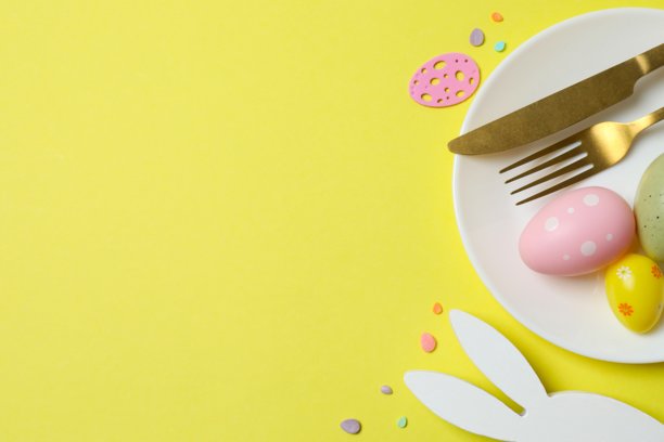 复活节快乐。彩色背景上的餐盘、餐具、彩蛋和兔耳朵的俯拍照片，留有空白空间图片下载