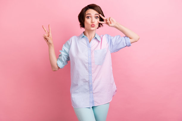 照片肖像：女子开心竖起V字手势，在粉彩色背景前送飞吻图片下载