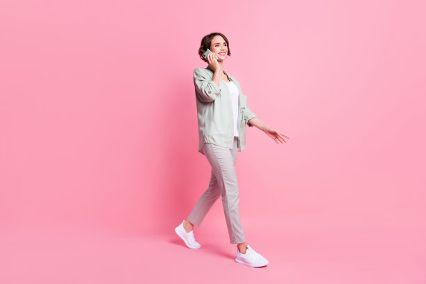 乐观波波头的年轻女子，身穿灰绿色衣服，在粉色背景下打电话，全尺寸照片图片下载