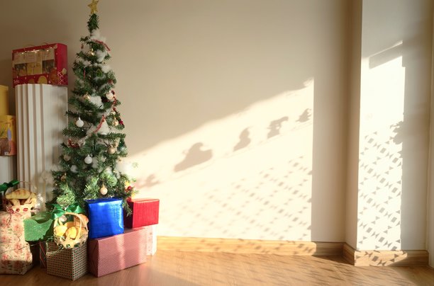 节日圣诞室内装饰，包括装饰好的圣诞树和摆放在大片空白墙旁的彩色礼品盒。温暖的自然阳光投下柔和的阴影，宽敞的空白墙壁提供了清晰的文字、标题、广告的复制空间。图片下载
