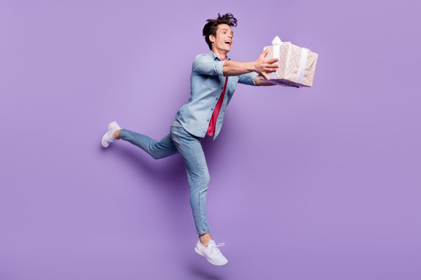 年轻男子生日派对礼物盒全尺寸侧身照片，快乐地笑着走或跑，孤立在紫色背景上图片下载