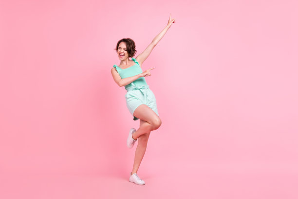 照片：一位穿着青绿色背心的漂亮年轻女子，面带笑容，兴奋地跳舞，背景为粉红色。图片下载