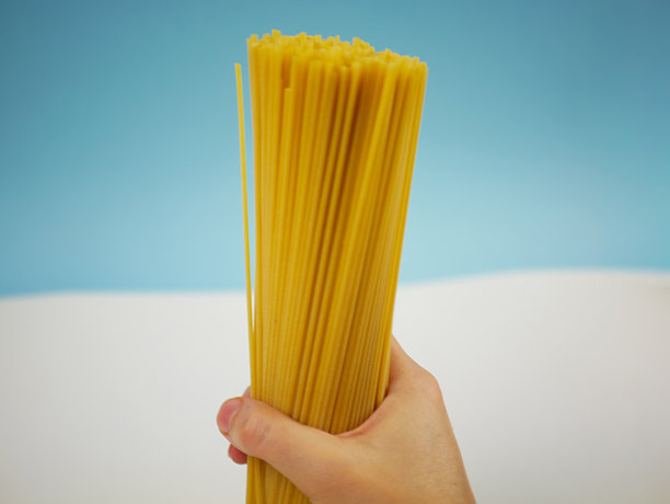 背景柔和的蓝色，特写一只手抓着一把长长的干意大利面，简洁的意式食材图片，适用于烹饪主题图片下载