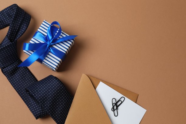 父亲节快乐扁平化概念。礼盒搭配丝带蝴蝶结、信封、优雅领带的俯视照片，背景为彩色。图片下载