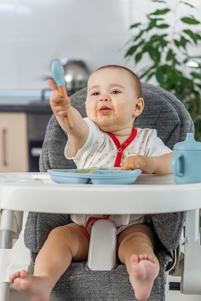 一个宝宝在自主进食时拿着勺子，场面有些狼藉。辅食添加。图片下载