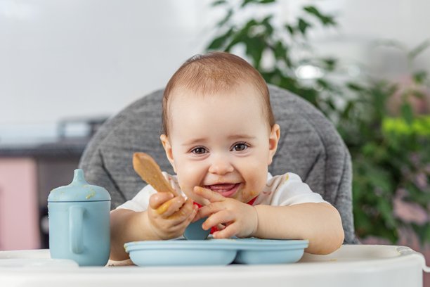 快乐的婴儿在用餐时间玩弄食物和勺子。辅食添加图片下载