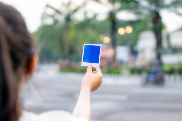街上，一只手正拿着蓝色的宝丽来照片纸，旁边是一台老式相机。图片下载