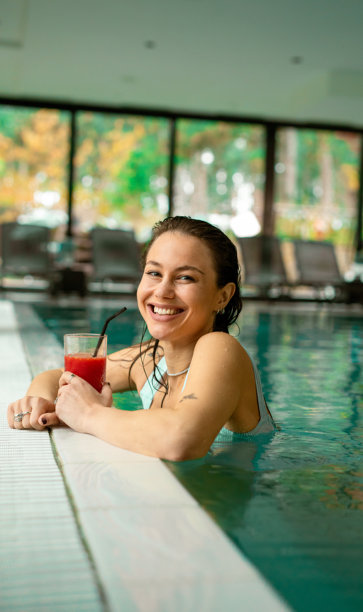 年轻女子在室内游泳池享受饮品。素材图片图片下载