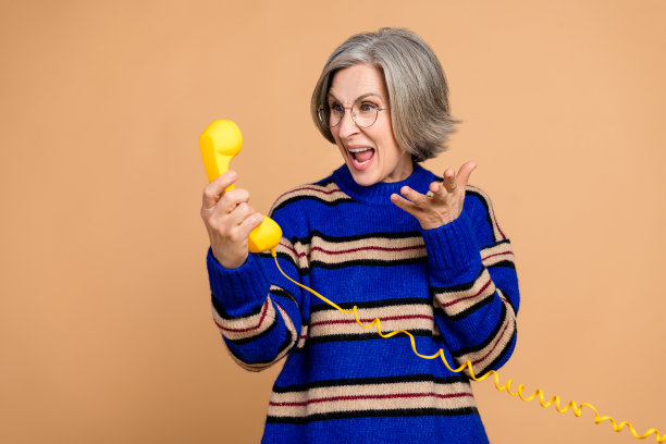 一位穿着蓝色条纹毛衣、使用黄色电话的成熟的女士正在微笑，用于广告和生活方式素材照片图片下载