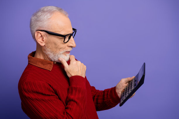 一位戴眼镜的老年男子穿着红色毛衣，在紫色背景前阅读计算器，这是一张时尚的商务生活方式图片图片下载