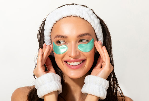 年轻女子戴着发带和护腕，使用眼部精华贴片进行美容护理，打造健康亮丽的肌肤图片下载