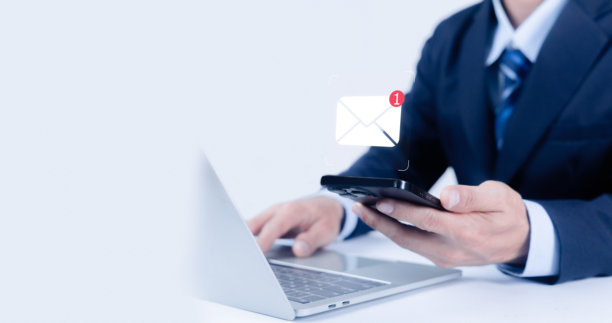 一位身穿海军蓝西装的人正在使用笔记本电脑，同时拿着一部智能手机。数字新消息图标阐释了商业沟通、数字通知和移动技术等概念。图片下载