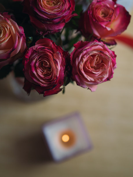 从正上方俯拍，一束粉色玫瑰花置于木桌上，旁边点燃着蜡烛，竖幅构图。图片下载
