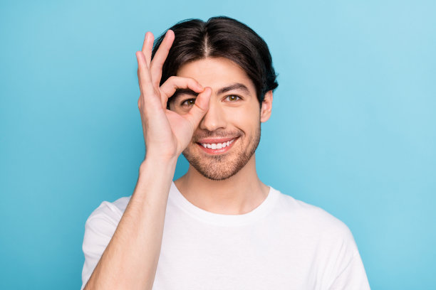 穿着白色T恤、戴着眼镜、摆出OK手势的千禧一代时尚棕发男子，在蓝色背景下的照片图片下载