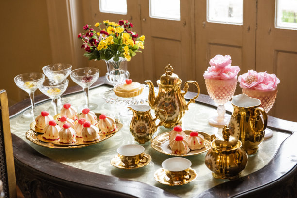 一张优雅的餐桌，摆放着精致的瓷器餐具，整体呈现出18世纪风格的精致复古感。画面色调温暖，以金色、粉色和花卉细节为主。自然、柔和的光线。图片下载