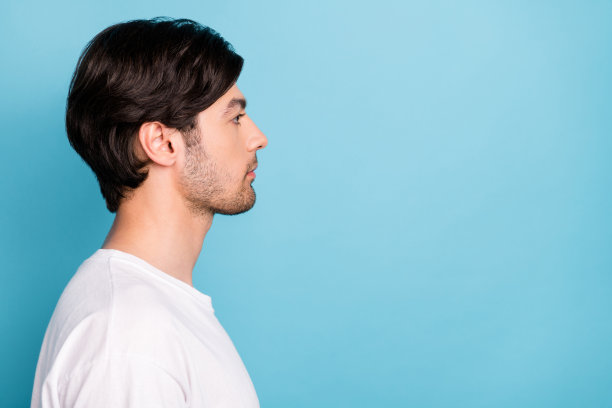 穿着白色T恤的年轻帅气男士的个人资料照片，目光望向空白处，在蓝色背景上孤立图片下载