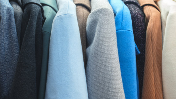 衣架上挂着一排大衣，其中蓝色大衣最为显眼。大衣颜色和款式多样，整张图片营造出一种整洁有序的氛围。图片下载