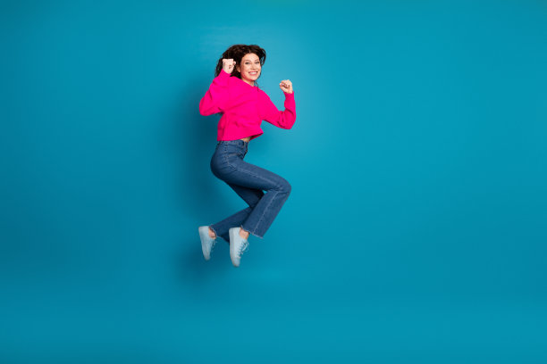 Young woman in pink knit sweater jumps with joy against a blue background for lifestyle fashion advertising and promotion图片下载