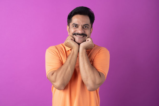 身穿橙色T恤的印度中年男性照片，孤立在紫色背景上图片下载
