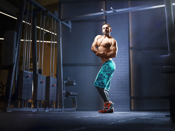 健身男性。身材健美的年轻男子在现代健身房摆姿势。运动。健身与健康概念。健美男子正在锻炼。肌肉发达的健身模特使用哑铃和杠铃锻炼的照片。图片下载