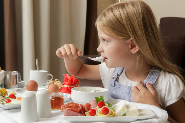 可爱的小女孩在吃早餐，谷物配酸奶，桌上摆着各种美味健康的菜肴选择图片下载
