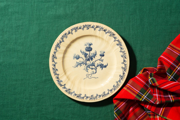 复古蓝色花卉盘子，搭配祖母绿背景，苏格兰格子布点缀，精致的餐桌布置细节。绿色背景。特写。俯视。图片下载