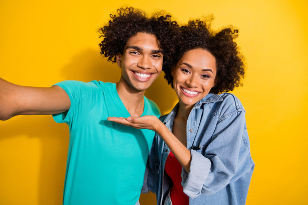 一张照片，画面中是一位皮肤黝黑的快乐男子和女子自拍，他们手牵手，面带微笑，背景为黄色。图片下载