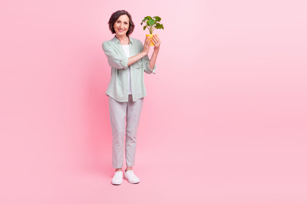 粉色背景下，一位积极的、未经修饰的年长者手持小植物，看向镜头，全尺寸照片图片下载
