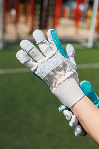 这张特写图片聚焦于绿色草地上的守门员手套，展示了其设计和在足球中的作用，同时也反映了运动员们所拥抱的当前运动服时尚潮流。图片下载
