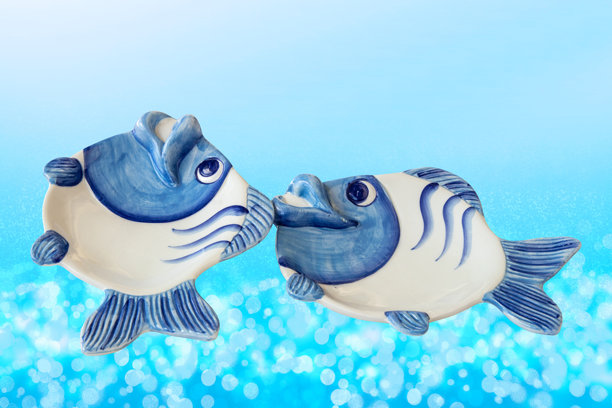 抽象蓝色水下背景上两条手绘的、鱼形空瓷碗的特写。陶瓷鱼形餐具。图片下载