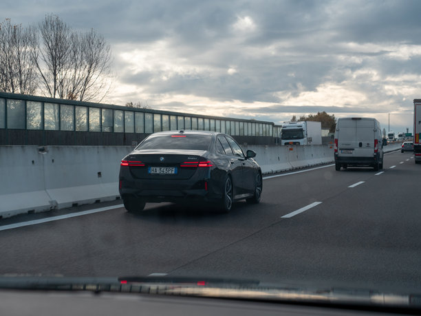 一辆黑色的宝马汽车在意大利的A4高速公路上行驶，天空多云，并遭遇了交通拥堵。图片下载
