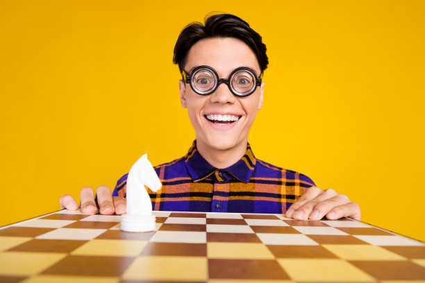 身穿格子服装、戴着眼镜的有趣时髦的青少年男孩，在孤立的黄色背景上笑着下棋的照片图片下载