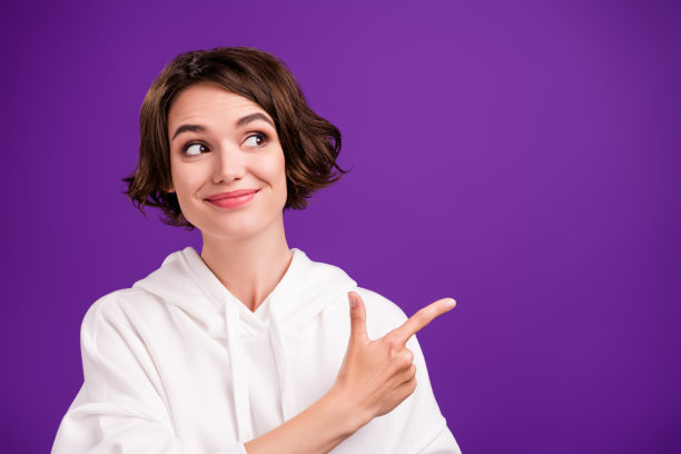 照片：迷人的漂亮年轻女子穿着白色毛衣，在紫色背景前送你飞吻。图片下载