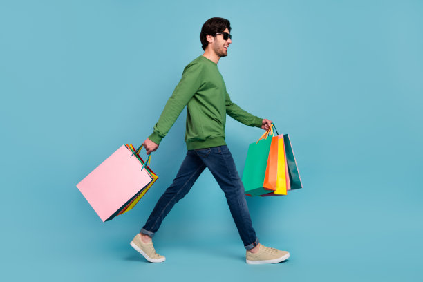 身穿太阳镜的微笑男士的全身侧面照片，他在黑色星期五去购物，背景是蓝色图片下载