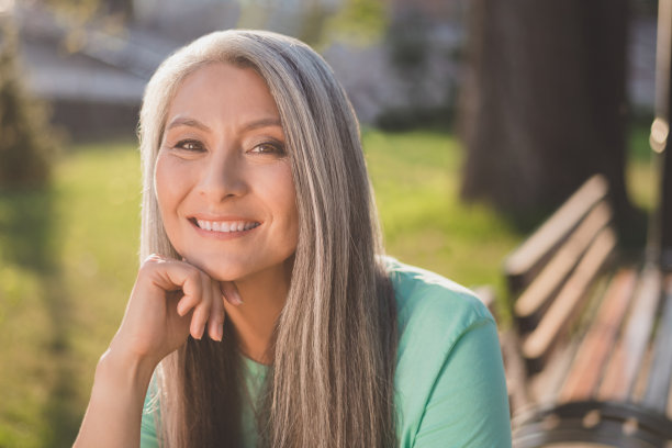 照片：一位富有想象力、深思熟虑的退休女士，穿着一件绿松石色T恤，望着晴朗的天空，背景是城市街景。图片下载