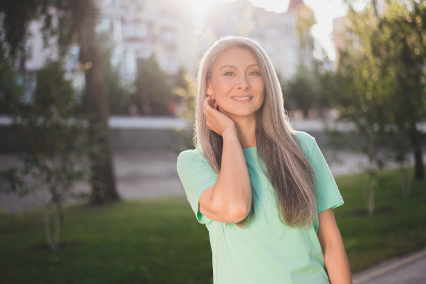 照片：一位梦想着、思索着、富有创造力的退休女士，身穿蓝绿色T恤，在城市户外仰望晴朗的天空。图片下载