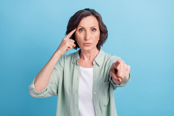 照片肖像，一位年长女性伸出V字手势，带着微笑，背景是孤立的粉蓝色图片下载