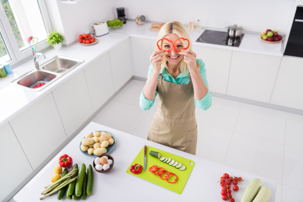 俯视镜头拍摄的成熟快乐的女厨师在厨房里穿着围裙做早餐的室内照片图片下载